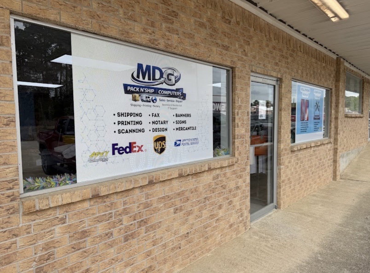 The MDG Pack N' Ship & Computers storefront on Pickens Road. The window graphic lists shipping, printing, scanning, fax, notary, design, banners, signs and mercantile, above the FedEx, UPS and United States Postal Service marks.